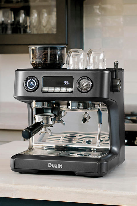                                                                            Black Dualit espresso machine on a kitchen counter with glasses in the background.                                                                     